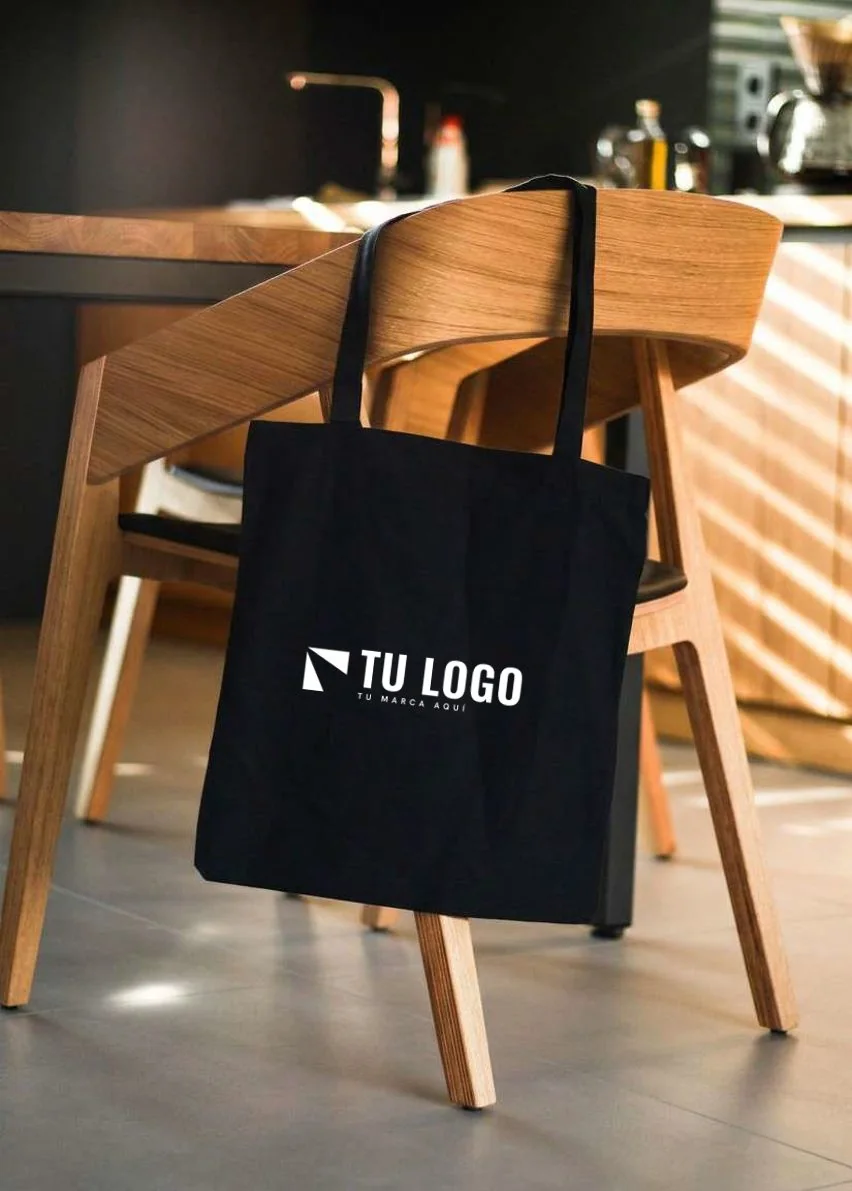 Tote de lona con el logo de una marca aplicado, colgado de una silla